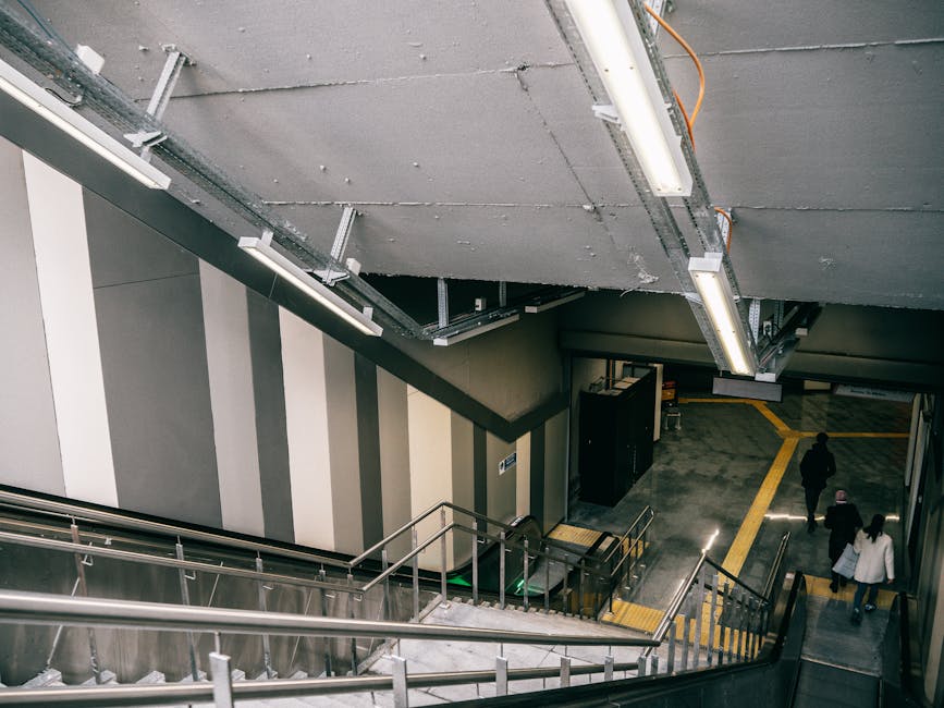 Inside a multi-level underground parking area near Wallington Station, with a staircase leading down to the pavement level where three individuals are walking. The environment features grey concrete w